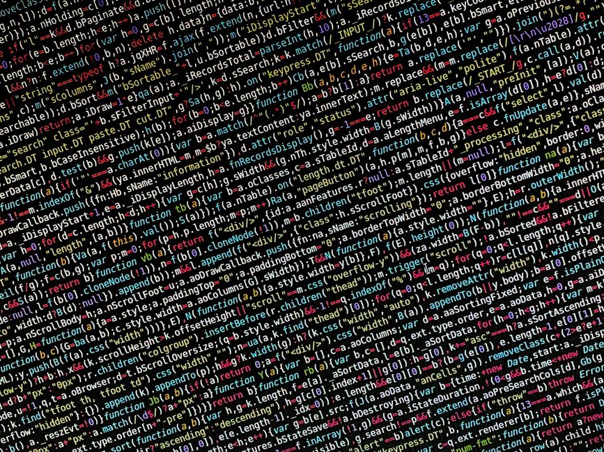 A photograph displaying a densely packed screen of computer code with multicolored syntax highlighting, featuring lines of programming in various colors such as red, blue, green, and white. The code i